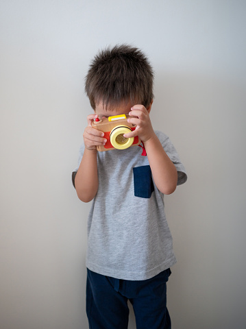 Two and a half years old baby boy having fun playing taking pictures with a small wooden toy camera. Imaginative play, creativity, learning and childhood development concepts