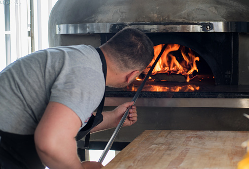 a pizzaiola pulls a pizza out of a Neapolitan oven