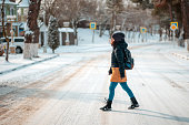 A young woman in a jacket and hat crosses a snow-covered empty street. Side view