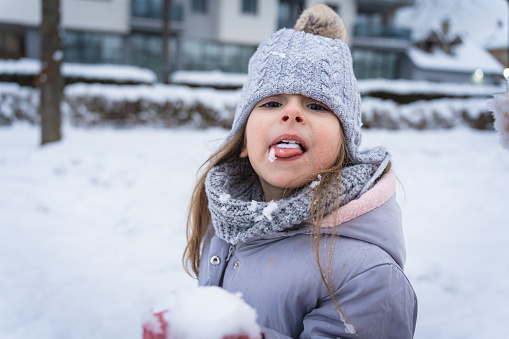 Portrait of an curious Caucasian toddler girl, licking the snowball, during an winter playtime