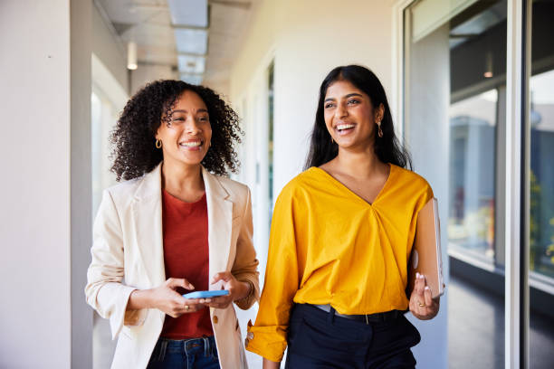 istock Two diverse young businesswomen laughing while walking in an office 1962648558