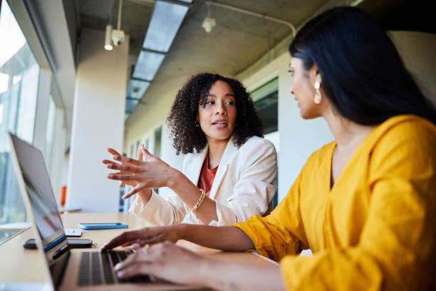 istock Two diverse businesswomen talking over a laptop at an office table 1962653578