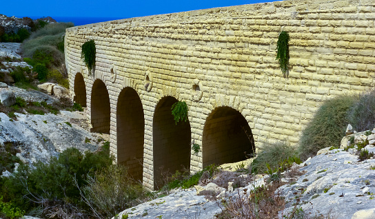 Dwejra, Gozo, Malta - September 14, 2012: An arched bridge road built with globigerina limestone stones like an aqueduct crossing the valley