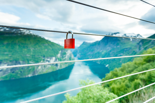 Tourism vacation and travel. Red love lock padlock on bridge and mountains, view over magical Geirangerfjorden from Flydalsjuvet viewpoint, Norway Scandinavia.