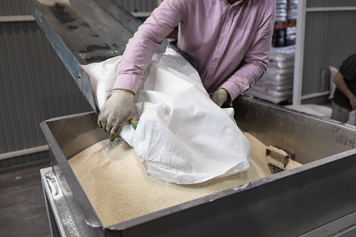 A worker pours a bag of sugar onto a conveyor line for further processing