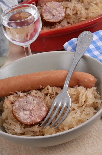 Sauerkraut plate with a frankfurter and a slice of morteau sausage with a fork and a glass of water close-up