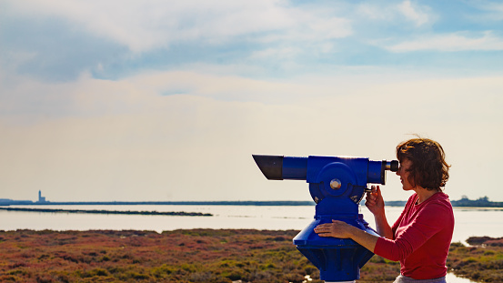 Woman using sightseeing binoculars, tourist telescope, overlooking Las Salinas landscape in Cabo de Gata Nijar Natural Park, Andalucia Spain. Place to visit. Tourism