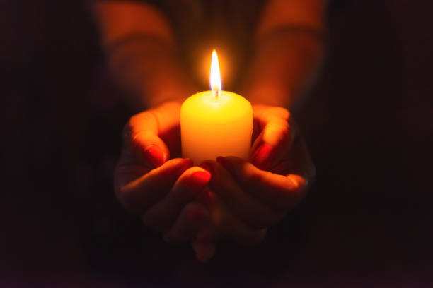 istock Candle in female hands on black dark background.Prayers candle in hands. 1962719635