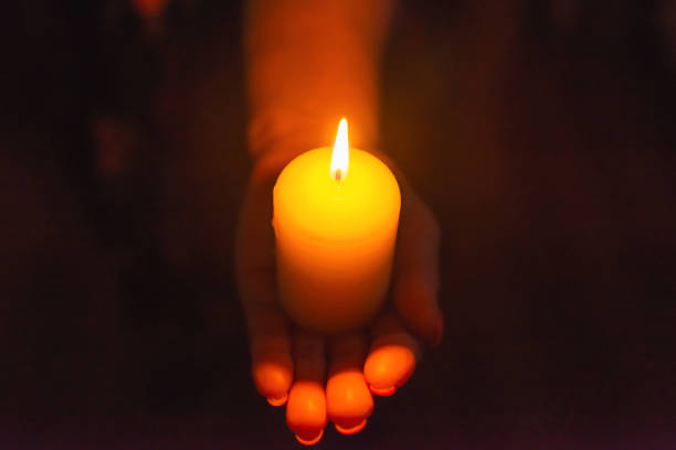 istock Candle in female hands on black dark background.Prayers candle in hands. 1962720140