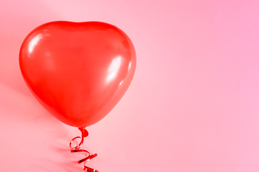 One red heart-shaped balloon lies in the left on a pink background with copy space on the right, flat lay close-up.