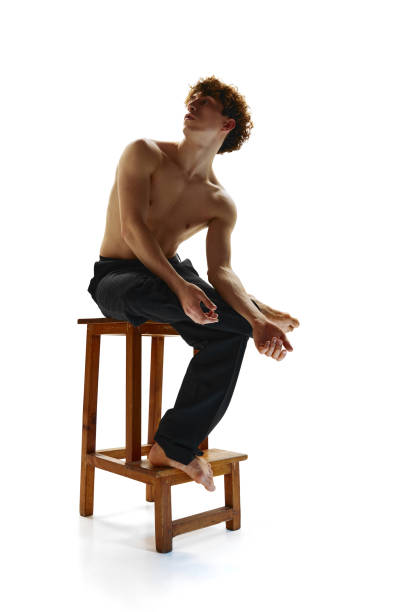 мускулистый мужчина без рубашки с обнаженным торсом позирует сидящим на табурете на белом студийном фоне. мужчина-модель с кудрявыми волос - motion art naked studio shot стоковые фото и изображения
