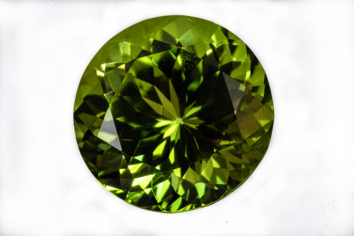 Green faceted peridot gemstone. Round, brilliant cut. White background.