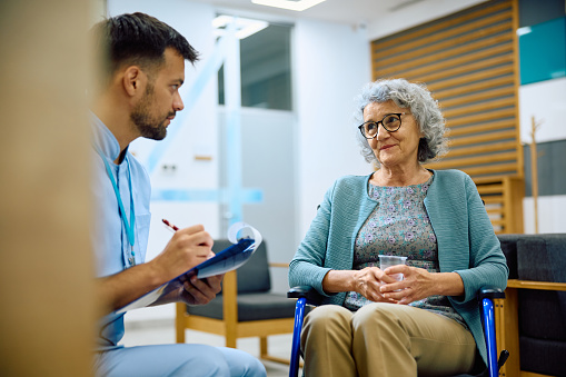 Medical technician writing data while communicating with senior female patient at the clinic. Copy space.