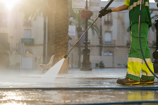 An unrecognizable worker uses a high-pressure water cleaner to remove dirt in the street.