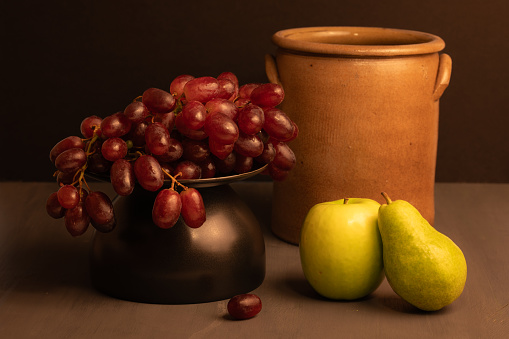 Still life image with red grapes on a plate next to an apple and a pear.