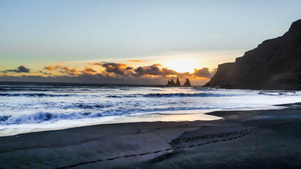 istock the sun sets over the ocean on a beach next to rocks and cliffs 1962853967