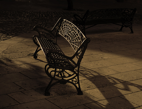 a wrought iron park bench in a plaza in the late afternoon light, Ronda, Spain