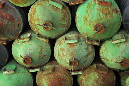 empty, rusted and weathered cans used for storing olive oil after it's been processed, stacked up along a wall outside of the factory, in the Sierra del Pinar foothills in Andalusia, Spain