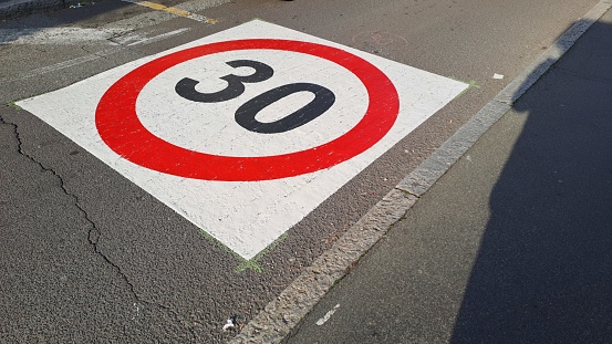 One triangle traffic sign with red border colour indicating 10 percent downhill gradient and other square marking beginning of residential district with start point of reduced speed zone of 30 km.