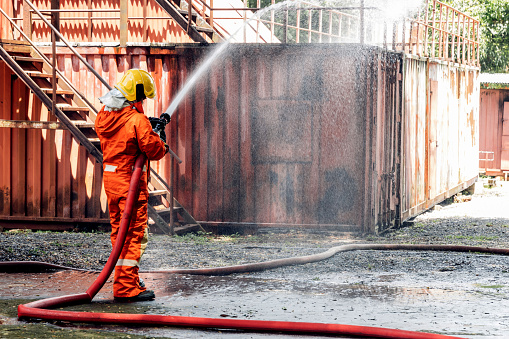 Close-up showing a person pointing the nozzle of a fire extinguisher at the base of a large fire.