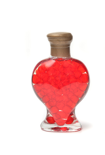 Closeup of a heart shaped glass bottle with red liquid balls symbolizing a love potion for Valentine's Day.