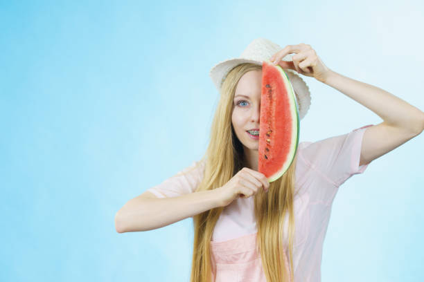 Happy cheerful teenage girl ready for summer wearing sun hat holding sweet fruit red juicy watermelon, on blue