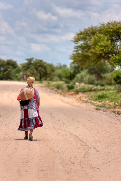 mujer africana basarwa caminando por un camino de tierra en la aldea tradicional - khoikhoi woman fotografías e imágenes de stock