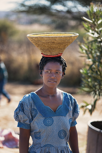 African woman carry waved basket with grains on her head, food for the the children, in the traditional way.