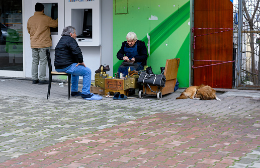Man shining shoes. His customer sits on a stool with his feet raised. Istanbul, Turkey. 01-26-2024.