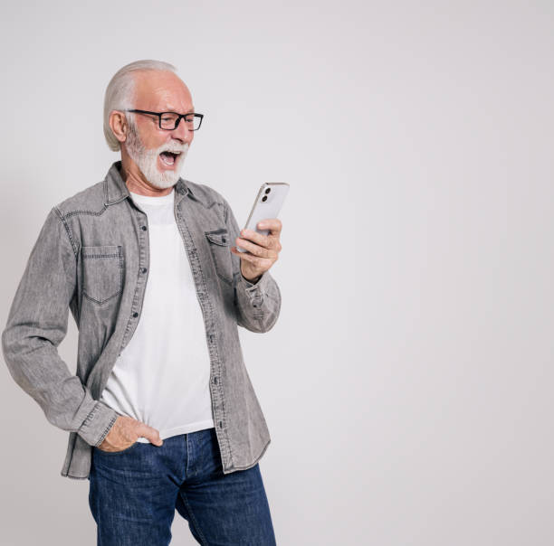 istock Senior businessman reading message over mobile phone and screaming ecstatically on white background 1962962597