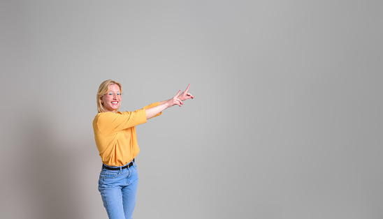 Smiling saleswoman with arms raised pointing at new product and marketing on white background