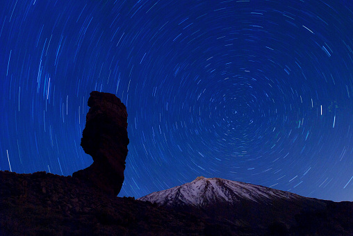 the Roque Cinchado at night with circling stars in the clear night sky and the summit of Pico de Teide, Tenerife, Canary Islands, Spain