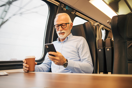 Senior businessman using his mobile phone while traveling with train and  drinking coffee
