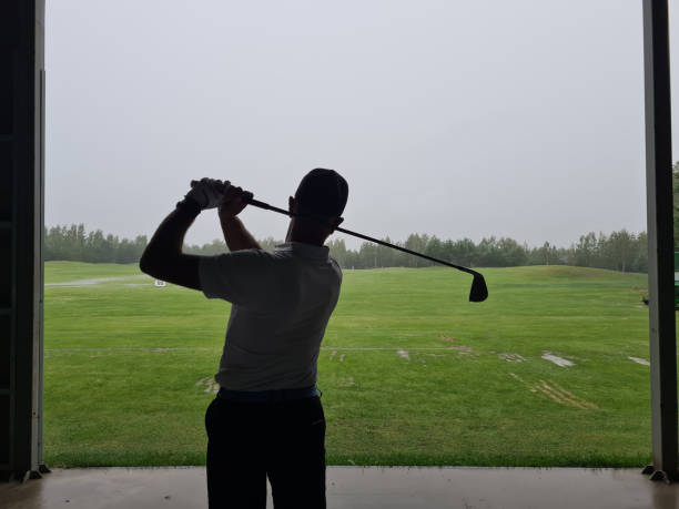 un homme joue au golf sur un champ de tir sous un toit - putting down photos et images de collection