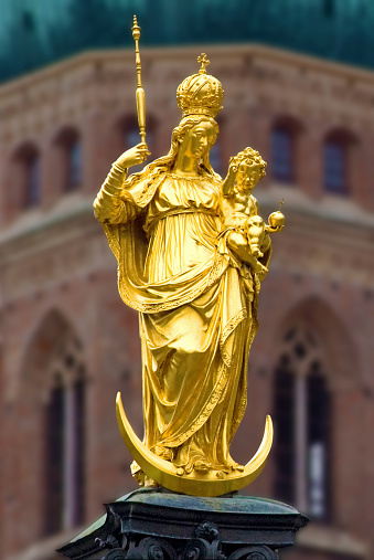 golden Statue of Virgin Mary with Jesus as a child, a tower of catholic church Liebfrauendom or Frauenkirche in background, Mary is the Patrona Bavariae, the Patron of Bavaria, Marienplatz, Munich, Upper Bavaria, Germany, Europe