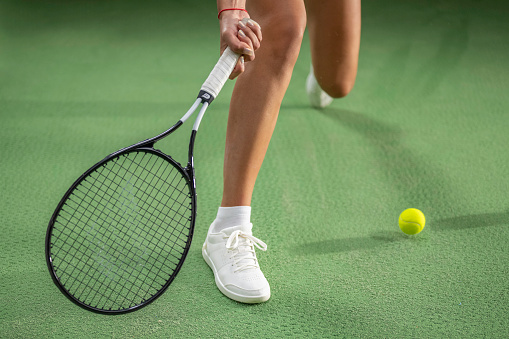 Female tennis player doing ground stroke with racket, legs in white sneakers medium shot