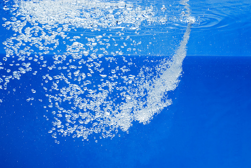 a thin jet of water penetrates the water surface and produces many air bubbles in the blue water of an aquarium