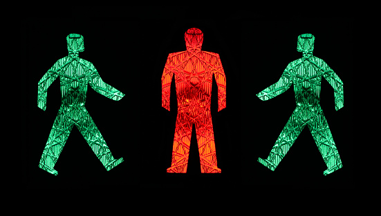 two green traffic light men walking towards a standing red one