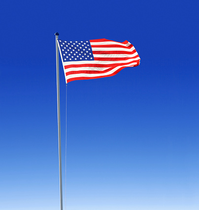 the national flag of the United States of America, USA, stars and stripes, on a flag pole flapping fluttering in the wind, blue sky