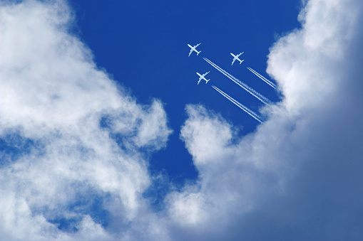 three airplanes high in the blue sky, flying formation with contrails between white clouds