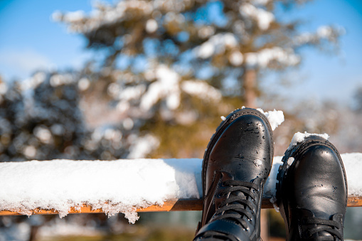 Female leaning her legs and feet on wooden fence after long walk on snowy day. Black winter boots on snowy fence outdoor. Copy space