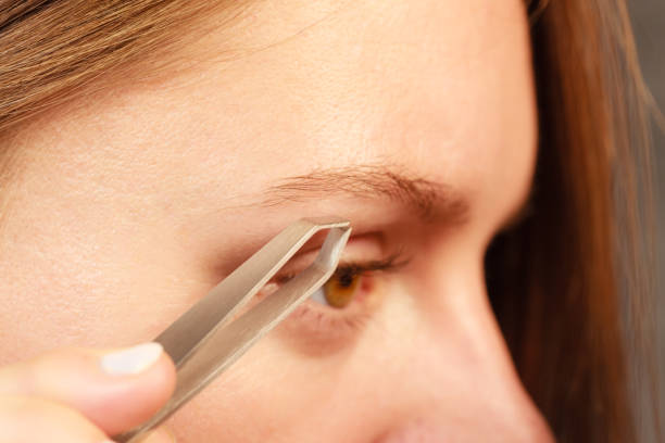 Woman plucking eyebrows depilating with tweezers closeup part of face. Girl tweezing eyebrows.