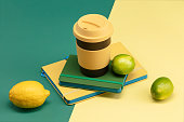 Coffee cup with lid, yellow and green notebooks, lemon and lime on a green and yellow background.