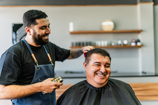 Barber cutting mature man customer hair's at barber shop