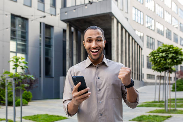 istock Young professional celebrating success with smartphone outside modern office 1963091950
