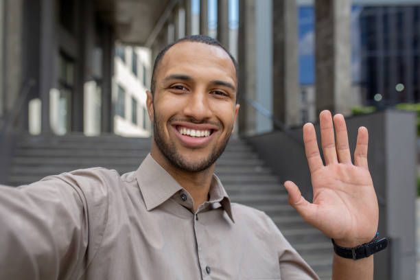 istock Friendly young man in casual attire waving hello in urban setting, expressing joy and approachability 1963091969