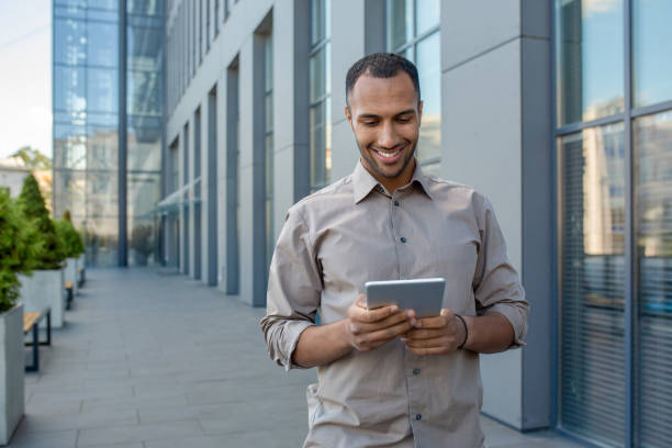istock Smiling businessman using tablet on sunny day at modern office exterior, happy at work 1963092247