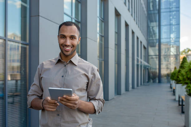 istock Confident young businessman with tablet walking by modern office building 1963092518