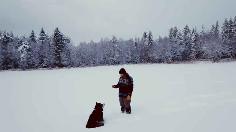 Man With His Alaskan Malamute Pet On Snowy Landscape In Norway - Wide