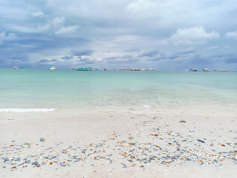 White beach with seashells and sand, blue water. There are boats in the middle of the sea. On the horizon at Koh Sichang, Thailand, beautiful sea